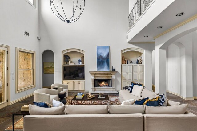 5902 Saratoga Cv, Austin, TX 78746 - living area featuring built in shelves, arched walkways, a chandelier, a towering ceiling, and a lit fireplace