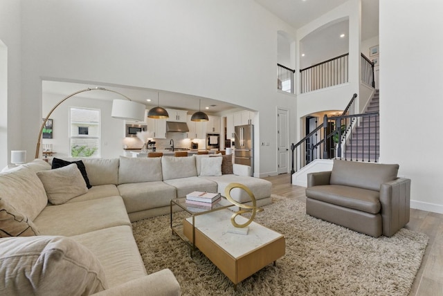 living room with arched walkways, light wood-type flooring, a towering ceiling, baseboards, and stairway