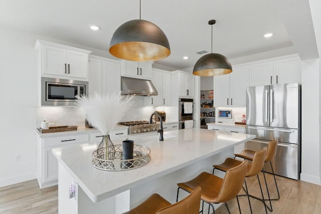 604 Buena Onda Way, Lakeway, TX 78738 - kitchen featuring appliances with stainless steel finishes, under cabinet range hood, light wood-style floors, tasteful backsplash, and recessed lighting