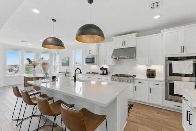 kitchen featuring appliances with stainless steel finishes, a breakfast bar area, a sink, under cabinet range hood, and recessed lighting