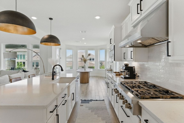 kitchen featuring appliances with stainless steel finishes, under cabinet range hood, a sink, a center island with sink, and backsplash