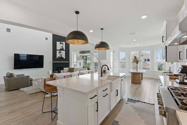 kitchen with a sink, light wood-type flooring, an island with sink, recessed lighting, and white cabinetry
