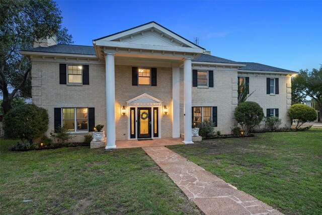 neoclassical / greek revival house with brick siding, a front lawn, and a chimney