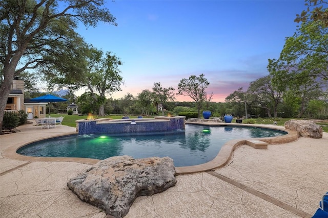 17700 N Rim Dr, Leander, TX 78641 - pool at dusk featuring a patio, a pool with connected hot tub, and an outbuilding