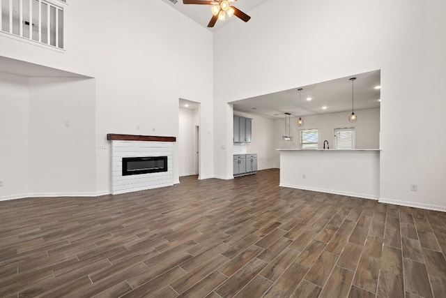 1100 Whipple Tree Trl, Georgetown, TX 78626 - unfurnished living room featuring a ceiling fan, dark wood-style flooring, a glass covered fireplace, baseboards, and a towering ceiling