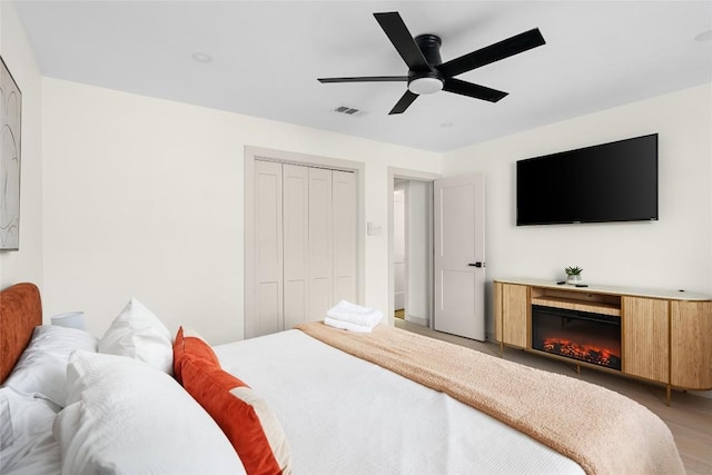 2209 Forest Bend Dr, Austin, TX 78704 - bedroom featuring a closet, a ceiling fan, light wood-style flooring, and a glass covered fireplace