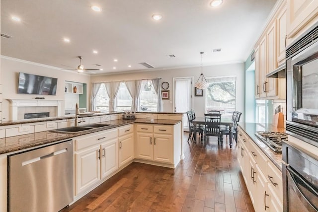 kitchen with stainless steel appliances, a sink, ornamental molding, a ceiling fan, and dark stone countertops