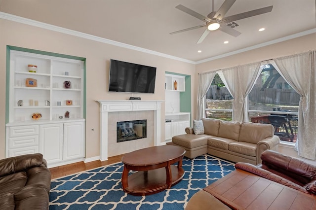 living area with a ceiling fan, ornamental molding, wood finished floors, a tiled fireplace, and recessed lighting