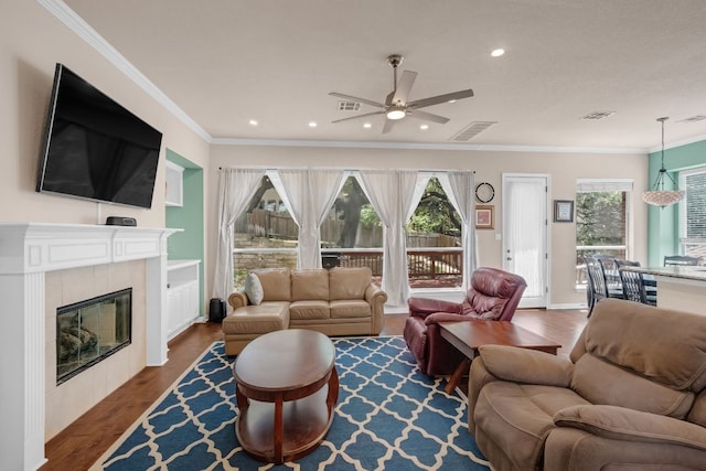 living room featuring a ceiling fan, wood finished floors, a tile fireplace, recessed lighting, and crown molding