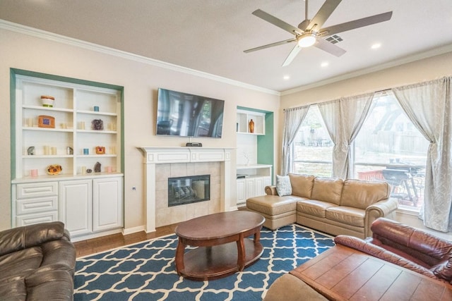 living room with crown molding, a ceiling fan, a tile fireplace, wood finished floors, and recessed lighting