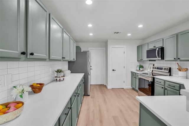 8921 Norwich Castle, Austin, TX 78747 - kitchen with stainless steel appliances, green cabinetry, light wood-style floors, decorative backsplash, and light countertops