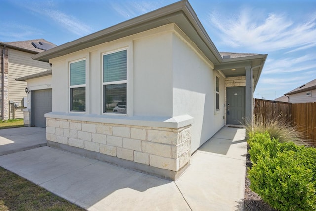 view of side of property featuring fence, driveway, a garage, and stucco siding