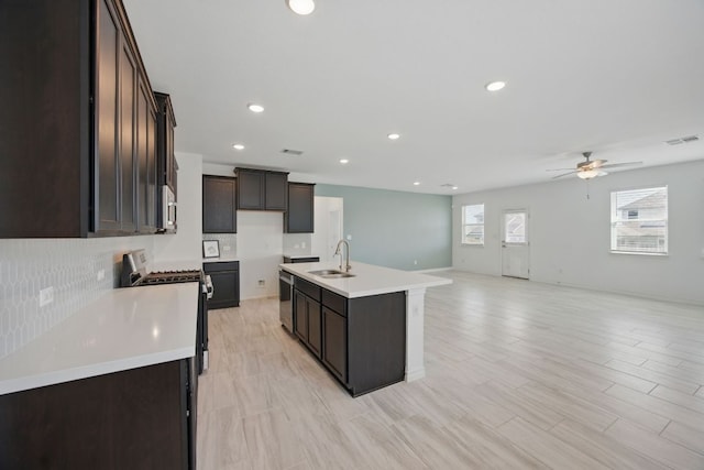 kitchen featuring appliances with stainless steel finishes, open floor plan, a ceiling fan, dark brown cabinetry, and decorative backsplash
