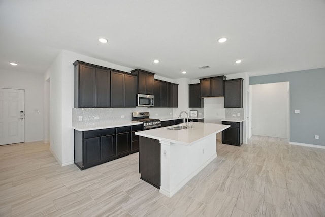 kitchen with stainless steel appliances, backsplash, a sink, light countertops, and an island with sink