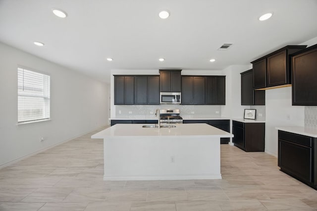 kitchen featuring stainless steel appliances, a sink, a center island with sink, backsplash, and recessed lighting