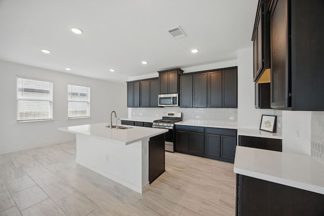 kitchen featuring stainless steel appliances, backsplash, light countertops, a sink, and a kitchen island with sink