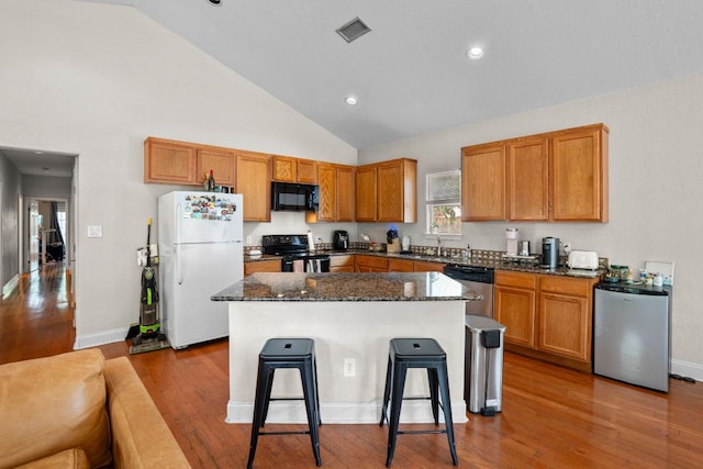 716 W 35th St, Austin, TX 78705 - kitchen with black appliances, a center island, a breakfast bar, wood finished floors, and dark stone countertops