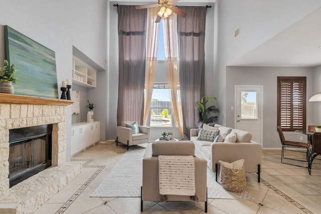 tiled living room featuring a towering ceiling, inlaid floor details, a ceiling fan, a fireplace, and built in features