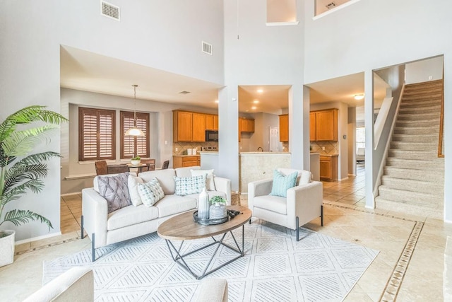 living room featuring light tile patterned floors, stairs, inlaid floor details, baseboards, and a towering ceiling