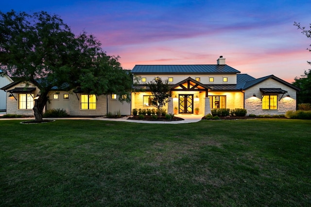 modern farmhouse style home featuring a standing seam roof, a chimney, stone siding, and a yard
