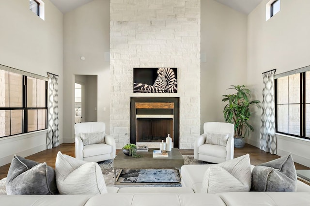 living area with high vaulted ceiling, a stone fireplace, baseboards, and wood finished floors