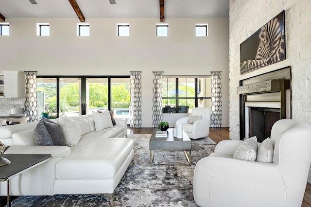 living area with a towering ceiling, beam ceiling, a fireplace, plenty of natural light, and wood finished floors