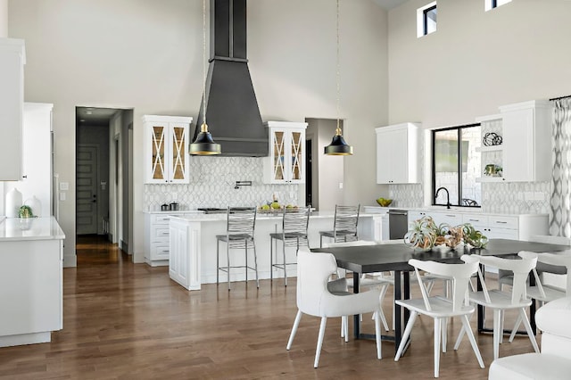 kitchen featuring a high ceiling, custom exhaust hood, a breakfast bar area, backsplash, and dishwasher