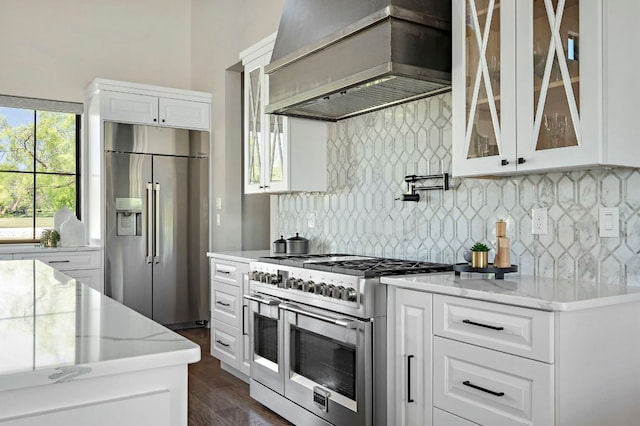 kitchen with appliances with stainless steel finishes, custom exhaust hood, glass insert cabinets, and white cabinets