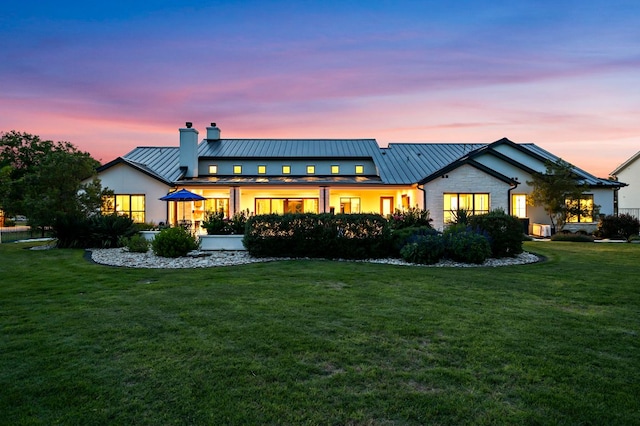 back of property at dusk featuring a standing seam roof, a chimney, and a yard