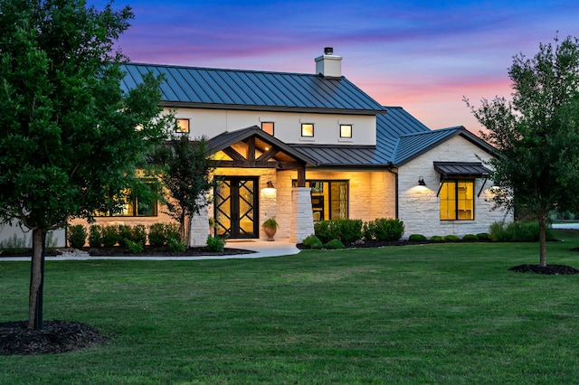 modern farmhouse featuring a standing seam roof, a chimney, metal roof, stone siding, and a front lawn