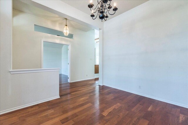 spare room with wood finished floors, a chandelier, and baseboards