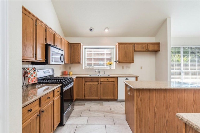 kitchen featuring stainless steel appliances, a sink, tasteful backsplash, brown cabinets, and lofted ceiling
