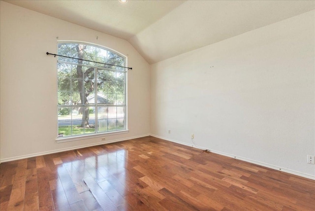 empty room with healthy amount of natural light, wood finished floors, vaulted ceiling, and baseboards