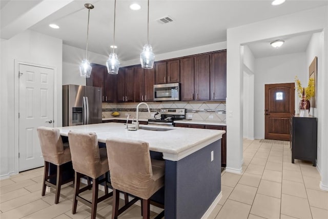 kitchen with appliances with stainless steel finishes, a sink, backsplash, a center island with sink, and dark brown cabinetry