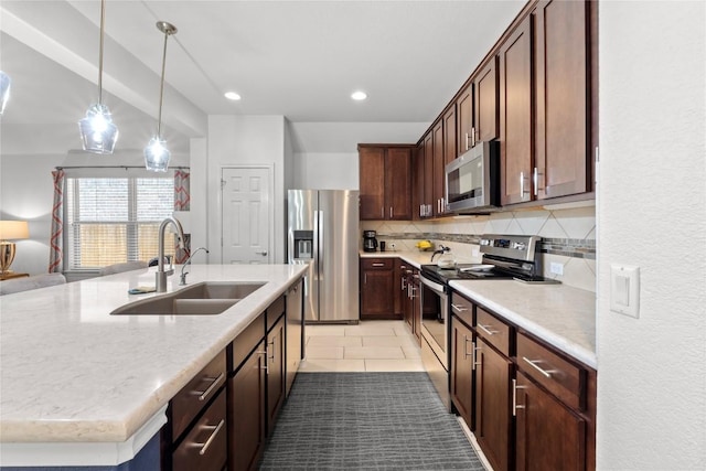 kitchen with appliances with stainless steel finishes, a sink, backsplash, pendant lighting, and a kitchen island with sink