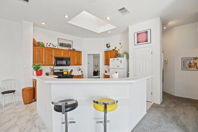kitchen featuring black microwave, freestanding refrigerator, a skylight, range with gas cooktop, and brown cabinets