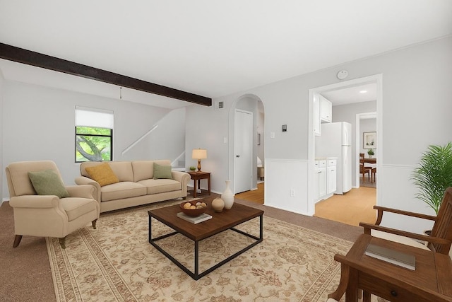living room with light colored carpet, arched walkways, stairs, beamed ceiling, and a wainscoted wall