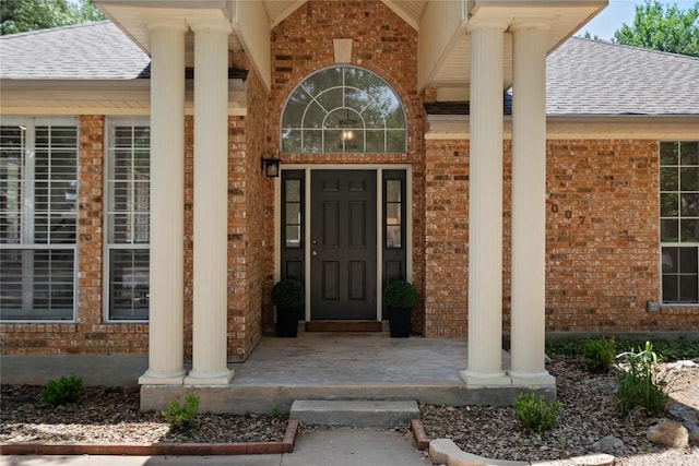 doorway to property with brick siding, a shingled roof, and a porch