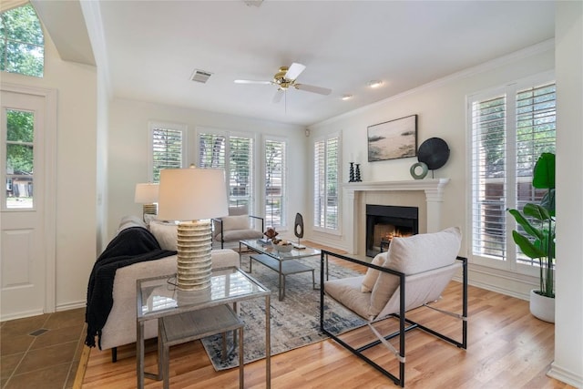 living area with plenty of natural light, a fireplace with flush hearth, ornamental molding, and ceiling fan