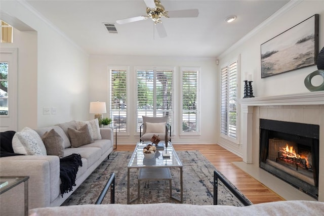 living area featuring wood finished floors, ornamental molding, a tile fireplace, a ceiling fan, and baseboards