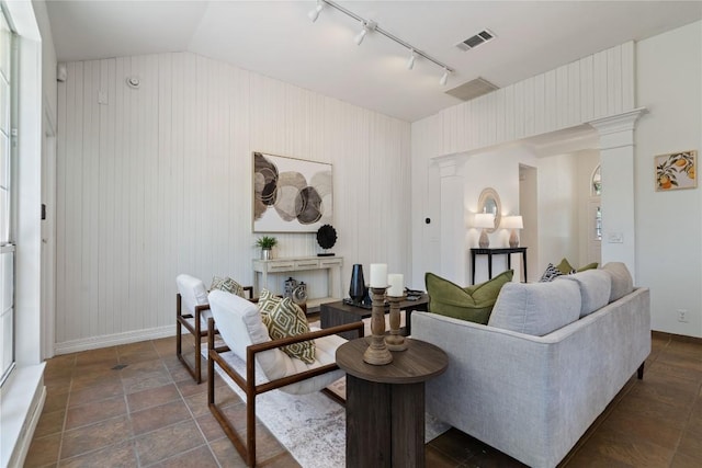 living area with rail lighting, vaulted ceiling, ornate columns, baseboards, and wooden walls