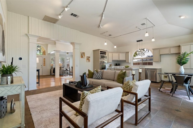 living room featuring ornate columns, track lighting, and a high ceiling