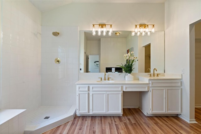 bathroom with wood finished floors, a tile shower, double vanity, and lofted ceiling