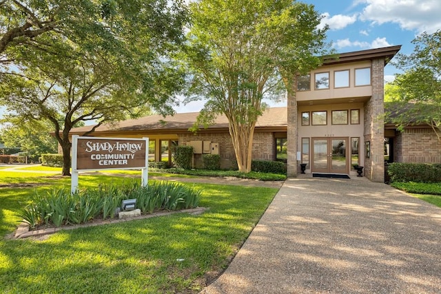view of front facade with french doors, a front yard, stucco siding, and brick siding