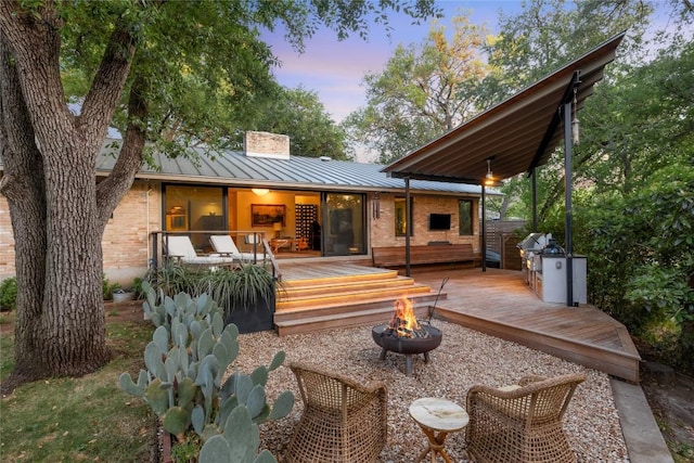 4504 Erin Ln, Austin, TX 78756 - back of house at dusk featuring a fire pit, a standing seam roof, a chimney, brick siding, and a wooden deck