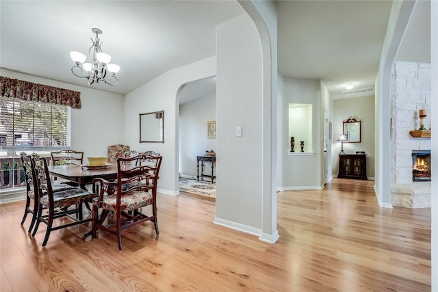 dining area featuring arched walkways, light wood finished floors, a chandelier, a fireplace, and baseboards