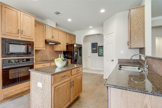 kitchen featuring black appliances, a sink, under cabinet range hood, arched walkways, and light brown cabinetry