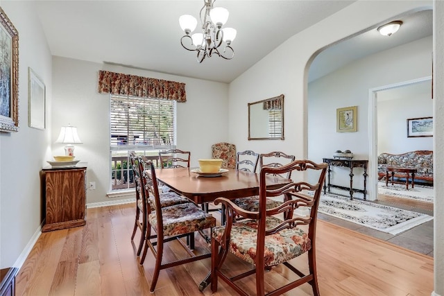 dining space featuring arched walkways, light wood-type flooring, a chandelier, lofted ceiling, and baseboards