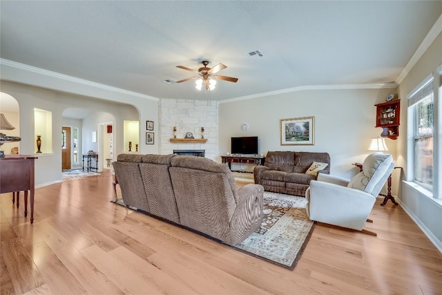 living room featuring arched walkways, ceiling fan, crown molding, light wood finished floors, and a fireplace
