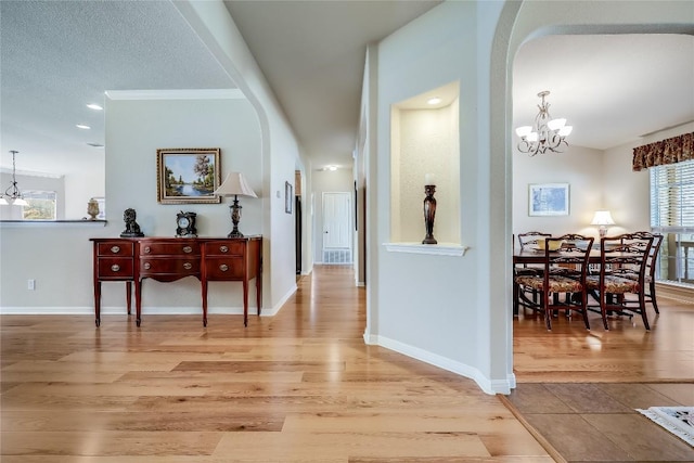 hallway with a chandelier, arched walkways, and light wood finished floors